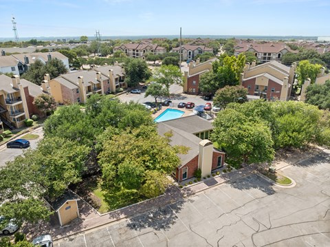A bird's eye view of a residential area with houses, trees, and a swimming pool.