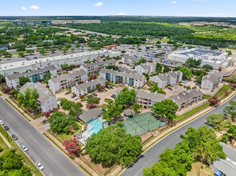 A bird's eye view of a residential area with houses, trees, and a pool.