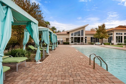 A pool area with a brick walkway and green lounge chairs.