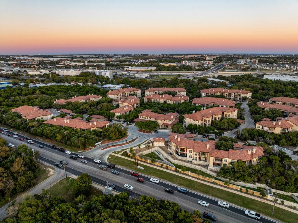 A sunset view of a highway with cars driving and apartment buildings on the side. at Bridge at Heritage Woods, Texas, 78753