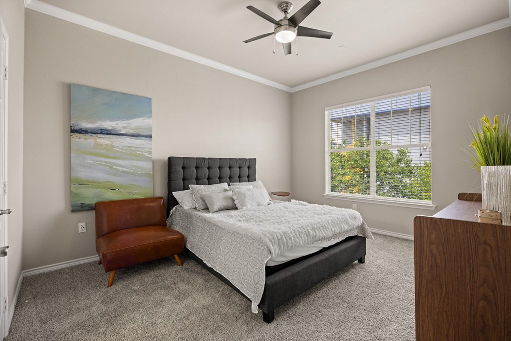 A bedroom with a bed, chair, and painting.
