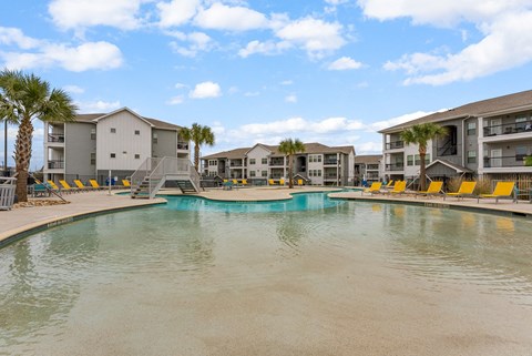 A swimming pool in front of apartment buildings with yellow lounge chairs.