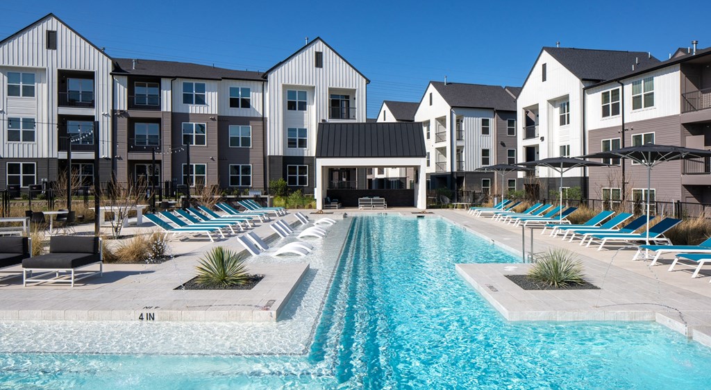 a swimming pool with lounge chairs in front of an apartment building