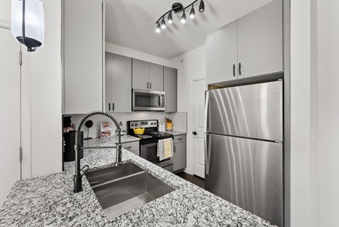 A kitchen with a stainless steel refrigerator and a sink with a black faucet.