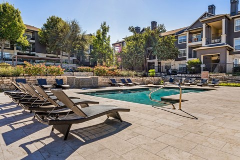 A pool surrounded by lounge chairs and trees. at Preserve at Rolling Oaks, Austin, 78728