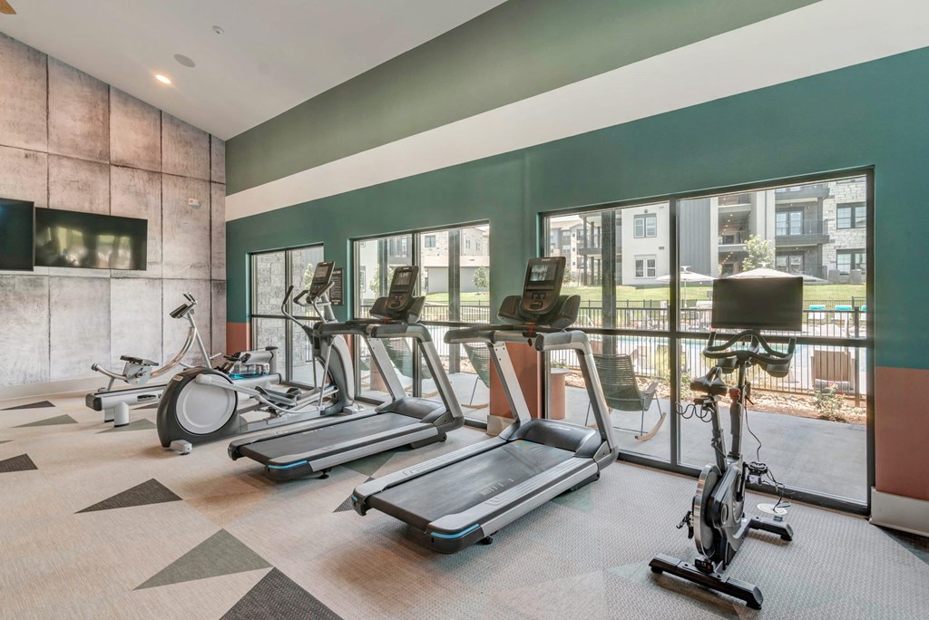 a gym with cardio equipment and windows with a view of a building