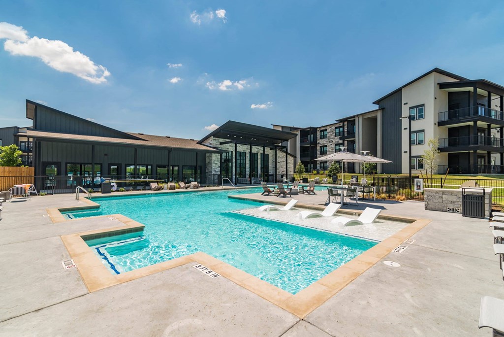 a swimming pool with lounge chairs and umbrellas next to an apartment building