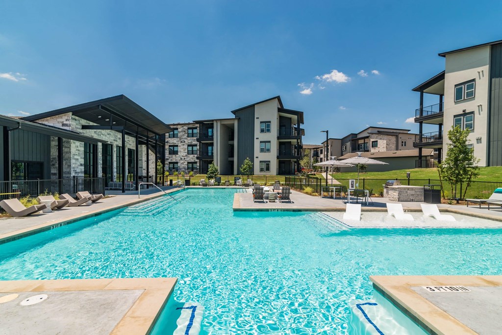 a large swimming pool with lounge chairs and apartments in the background