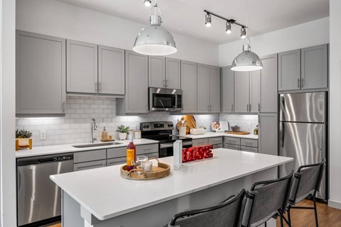 A modern kitchen with a white island and grey cabinets. at The Haywood Apartments, Texas