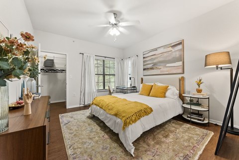 A bedroom with a bed in the center, a ceiling fan, and a painting on the wall.