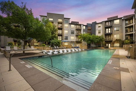 A swimming pool in front of apartment buildings at dusk.