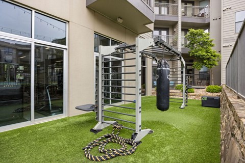A gym setup is placed on a small grassy area outside a building.