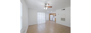 A room with a ceiling fan and a kitchenette in the background.