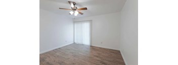 A room with a ceiling fan and light fixture, hardwood flooring, and a window with blinds.