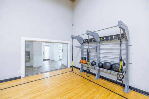 A gym with a wooden floor and a wall-mounted rack with weights.