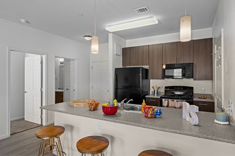 A kitchen with a black refrigerator and microwave, a countertop with a cutting board, bowl, and other items, and two stools.