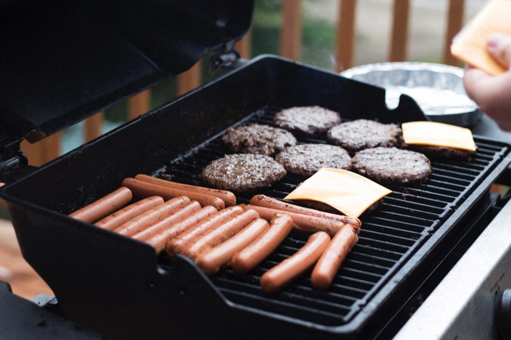 a grill with hot dogs and hamburgers and cheese on it