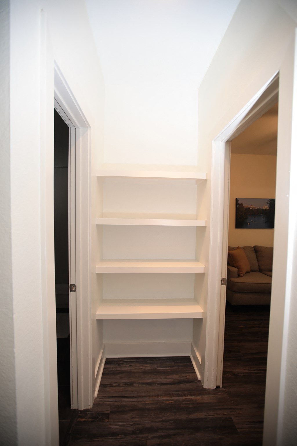 a small hallway with white shelves and a door into a living room