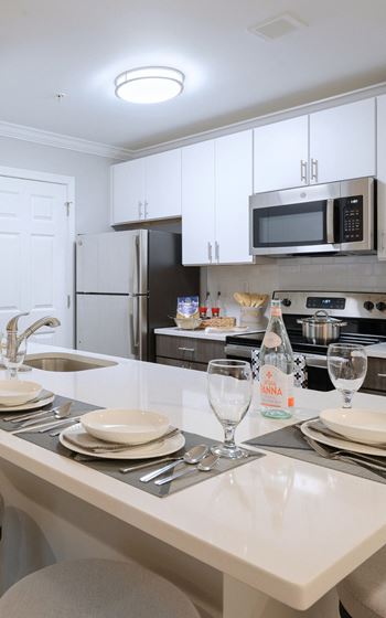 a kitchen with white cabinets and a white island with plates and glasses on it