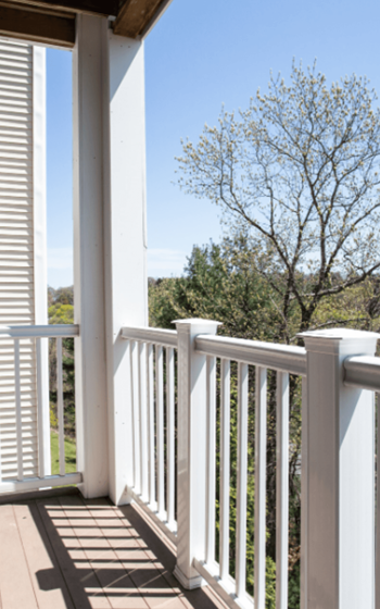 a picture of a balcony with white railing and a tree in the background