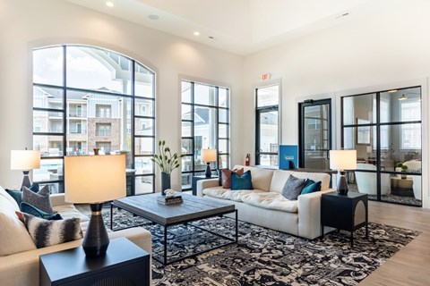 A well-lit living room with a large window, a sofa, a coffee table, and a side table with a lamp.