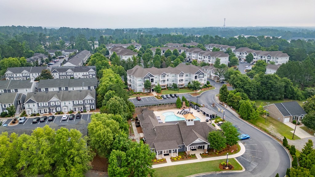 A bird's eye view of a residential area with houses, a swimming pool, and a parking lot at Ansley at Town Center Apartments, Evans, 30809