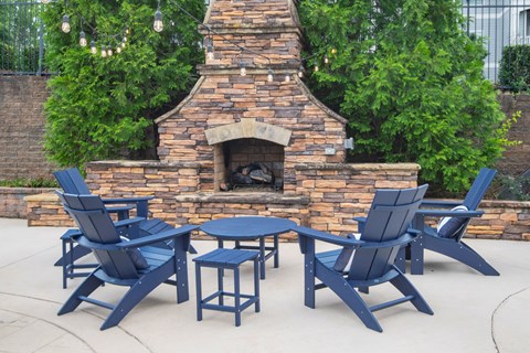 A set of blue chairs and tables are arranged around a brick fireplace.