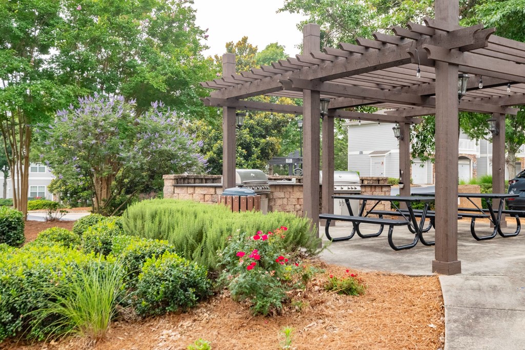 A wooden pergola with a sign on it is surrounded by greenery and a picnic table at Ansley at Town Center Apartments, Evans, Georgia