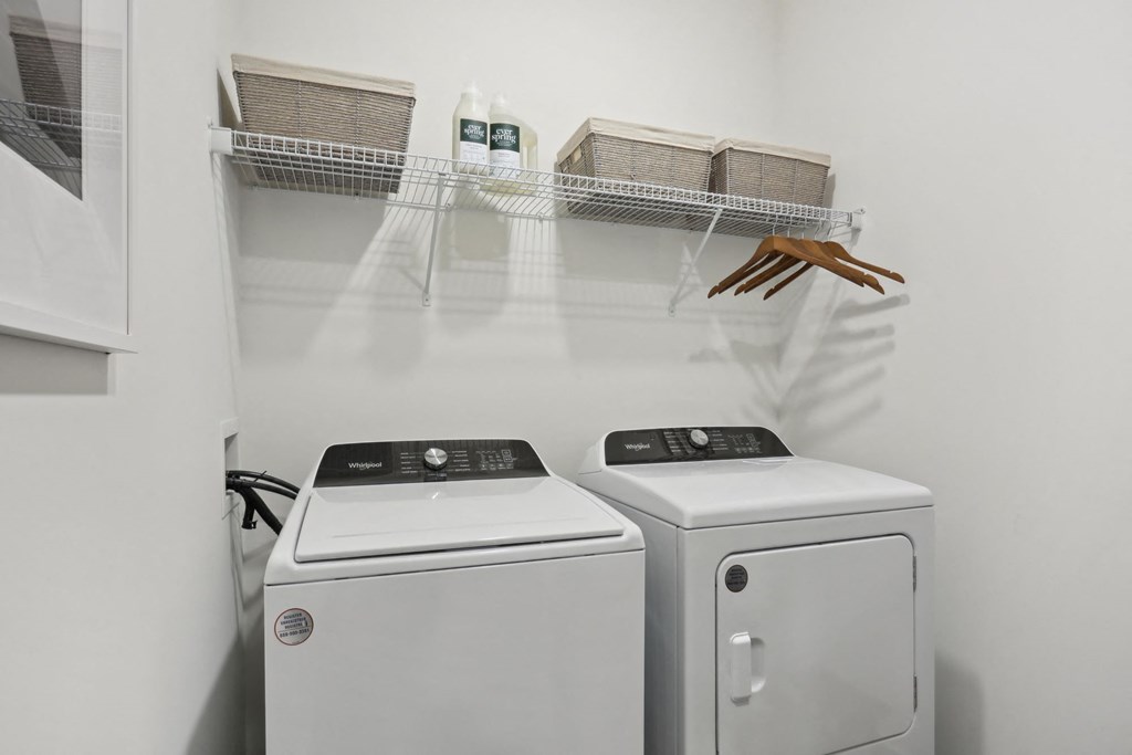 A laundry room with a washer and dryer and a shelf with baskets and a handbag. at Arcadia Cartersville Apartments, Cartersville, GA