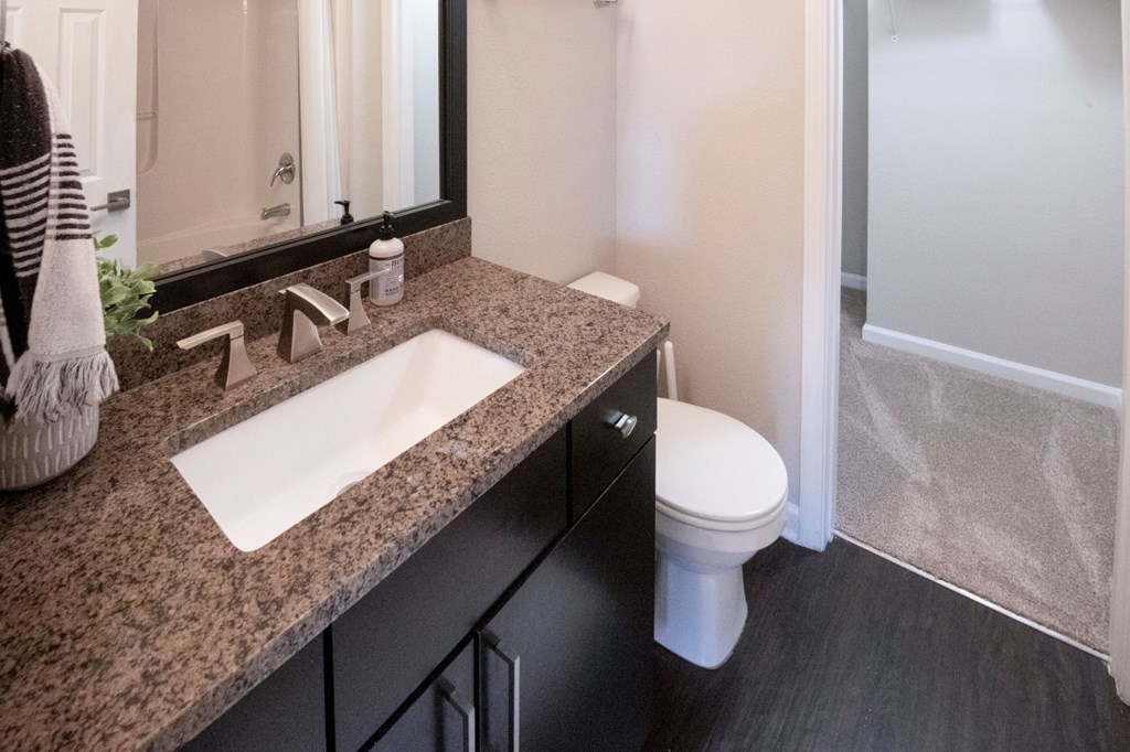 A bathroom with a sink, mirror, toilet and a shower.