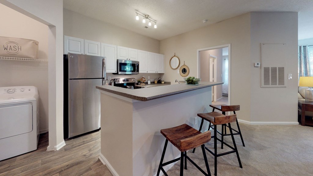 a kitchen with a breakfast bar and stools next to a washer and dryer at Autumn Park Apartments, Charlotte, 28262