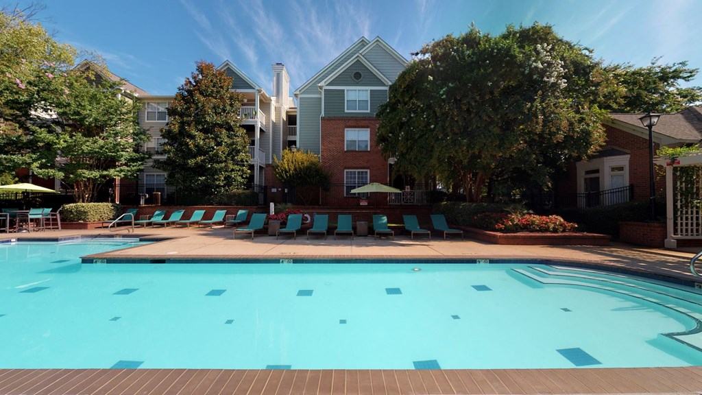 a swimming pool with lounge chairs and umbrellas in front of a brick building at Autumn Park Apartments, North Carolina