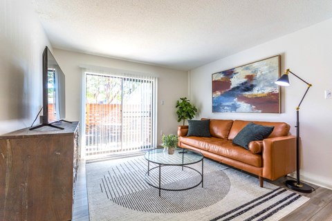 A living room with a brown couch, a glass coffee table, and a painting on the wall.