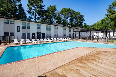 A large swimming pool with a wooden deck and lounge chairs in front of a building. at Century Apartments, Memphis, TN, 38117