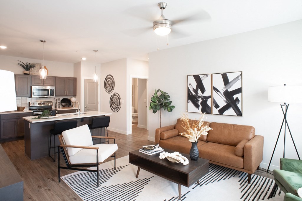 a living room with a ceiling fan and a kitchen in the background