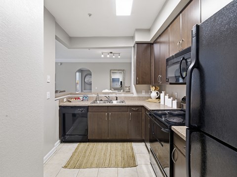 A kitchen with a black refrigerator and brown cabinets.