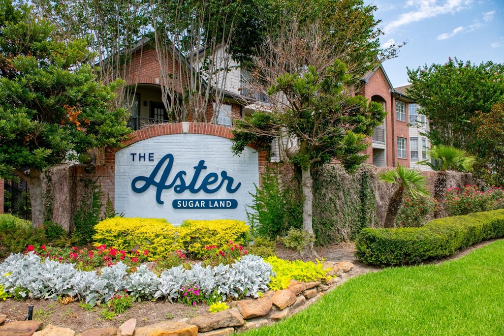 a sign that says the aster sugar land with flowers and bushes in front of it  at The Aster Sugar Land, Texas, 77498