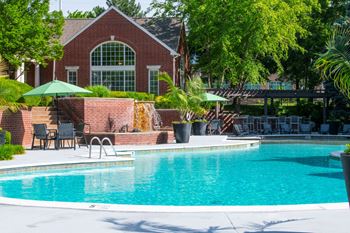 A pool in front of a house with a green umbrella.