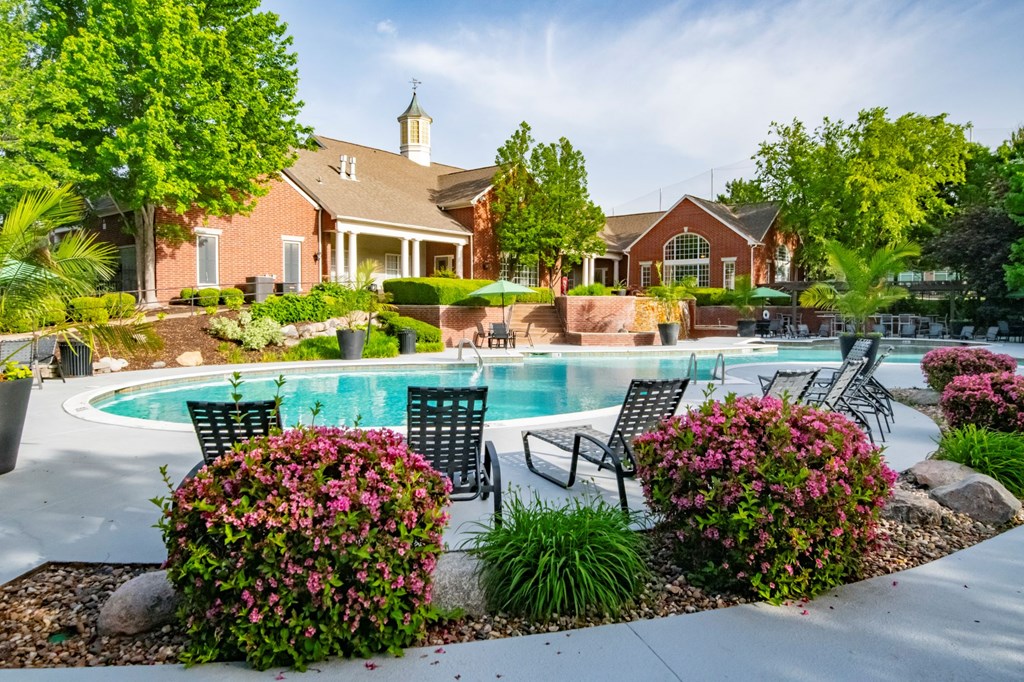 A pool surrounded by a garden with a house in the background. at Cambridge Square, Overland Park