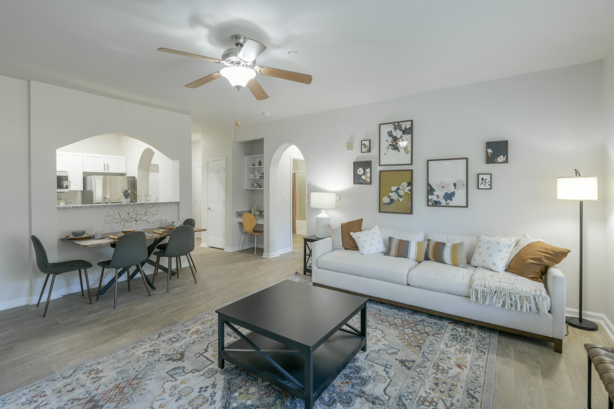 A living room with a white couch, a dining table with chairs, and a rug on the floor.