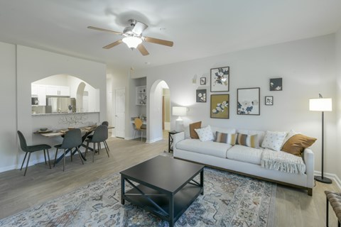 A living room with a white couch, a dining table with chairs, and a rug on the floor.