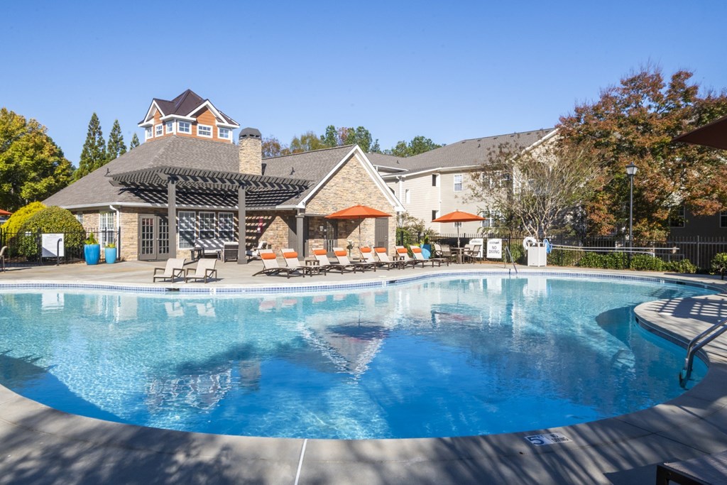 A large swimming pool in front of a house with a patio and sun loungers.