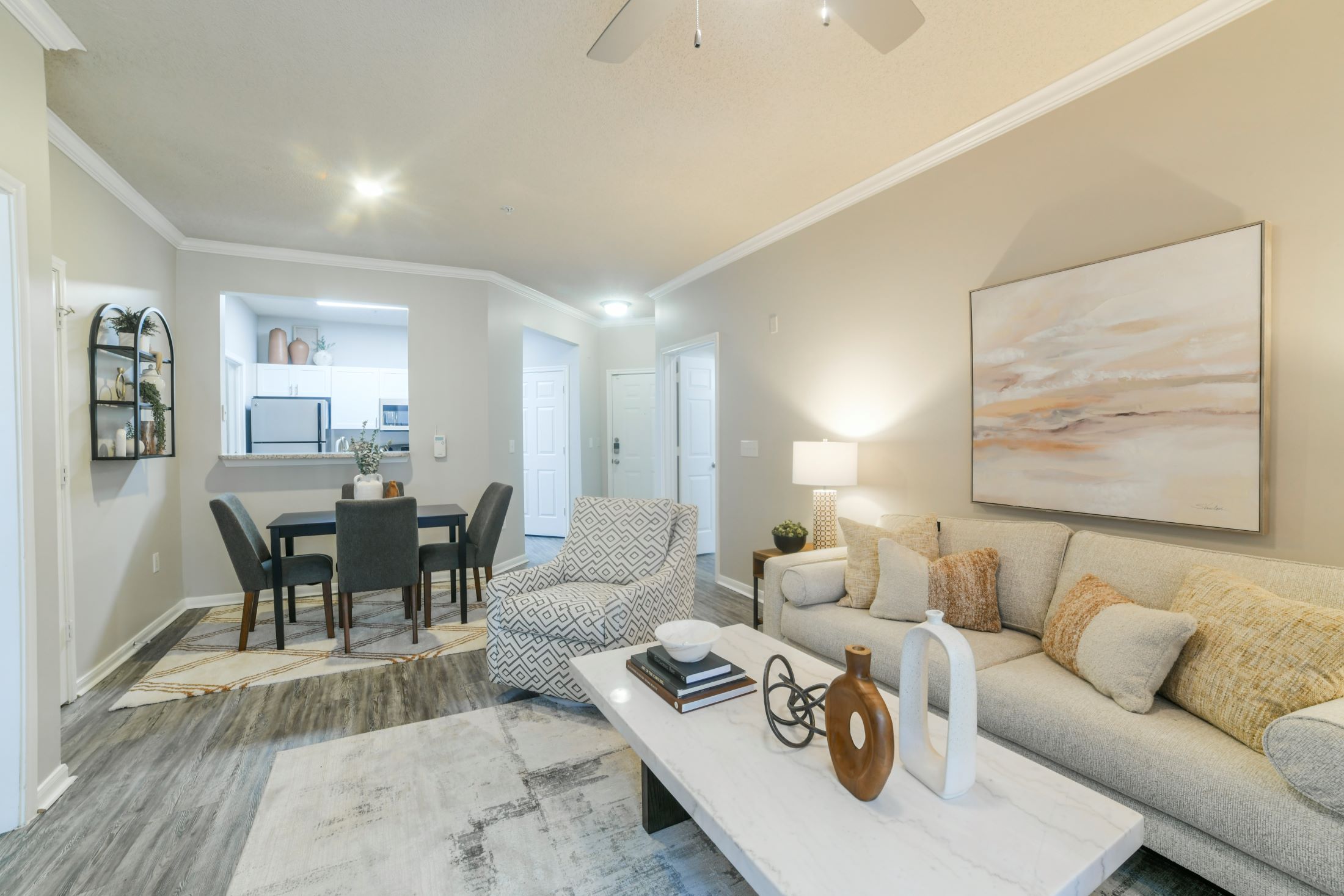 A modern living room with a grey couch, a dining table, and a painting on the wall.