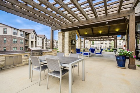 A patio with a table and chairs under a wooden pergola.