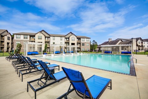 A pool area with sun loungers and apartment buildings in the background.