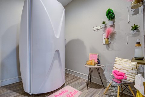 A white refrigerator stands in a room with a pink rug and a chair.
