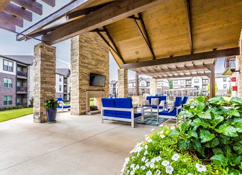 a covered patio with blue chairs and a fireplace at The McKenzie Park Apartments, Little Rock