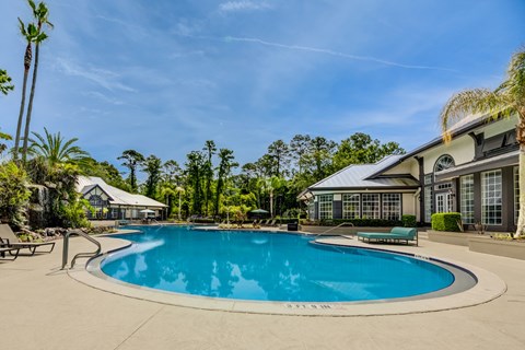 A large swimming pool surrounded by palm trees and a building.
