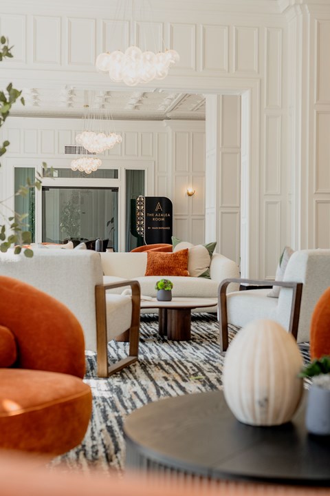 A living room with a white sofa, orange armchair, and a coffee table with a white pumpkin on it.