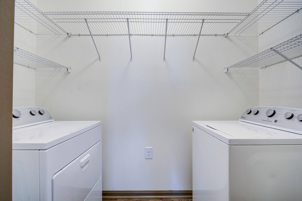 Two white ovens are under a wire rack.